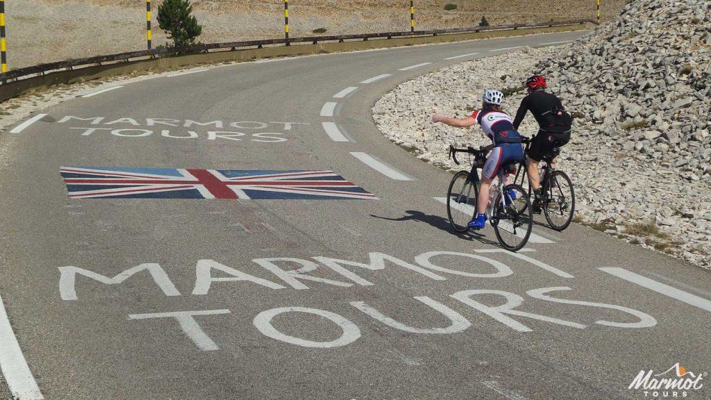 Two cyclists passing Marmot Tours logo and union jack on European road cycling holiday Mont Ventoux