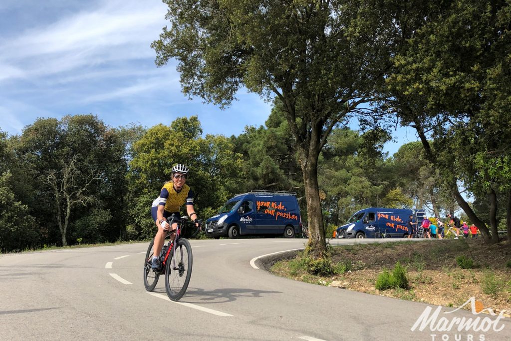 Cyclist descending with Marmot Tours support vehicles in background on fully supported group cycling holiday in Spain Catalonia