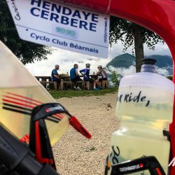 Group of cyclists enjoying rest at picnic bench with bike in foreground showing Raid Pyrenean Cyclo Club Bearnais tag on Marmot Tours road cycling challenge Pyrenees France