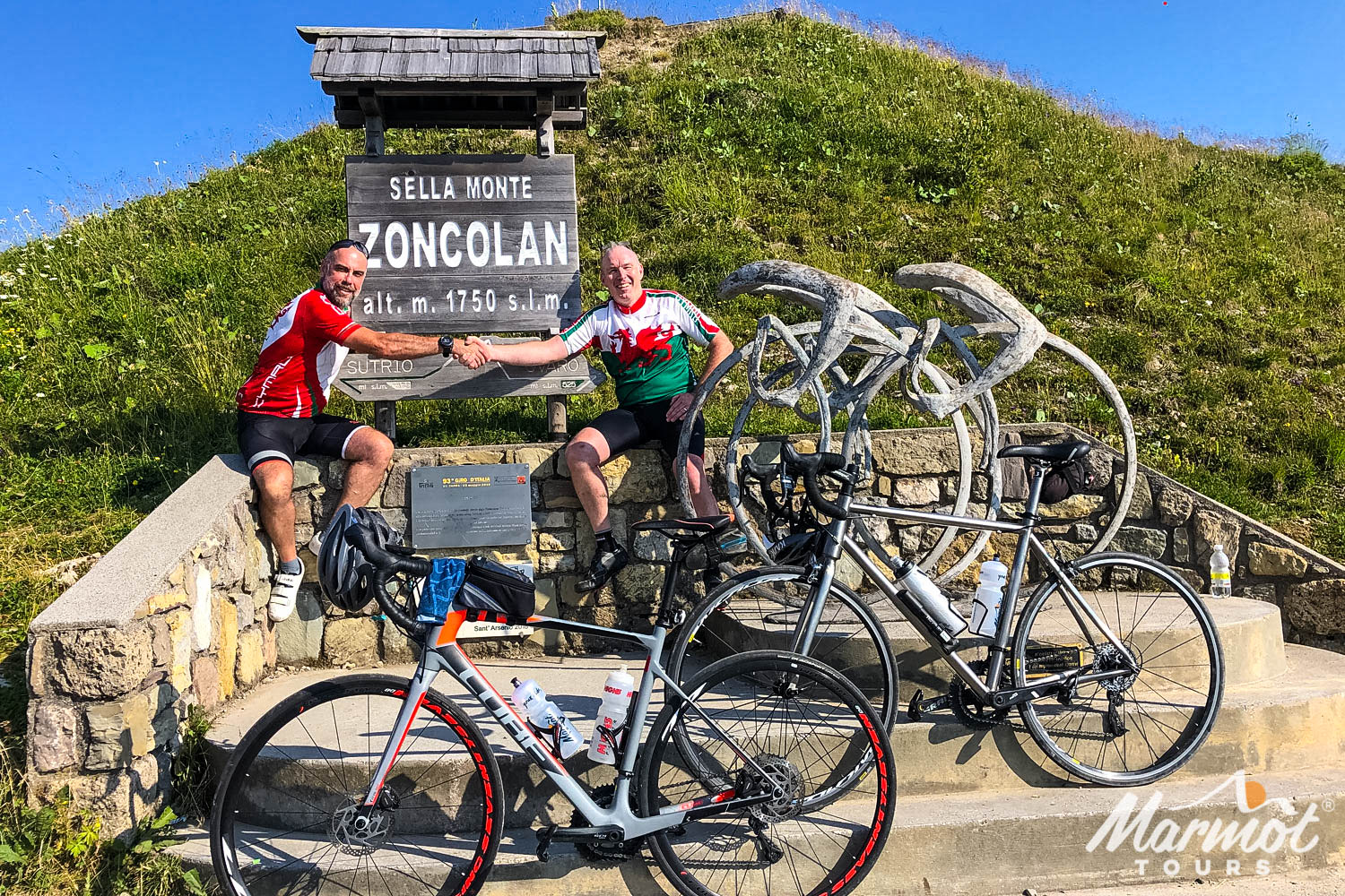Pair of cyclists shaking hands at summit of Monte Zoncolan on Marmot Tours fully supported road cycling tour of Slovenia