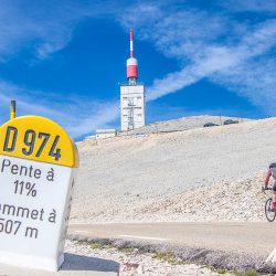 Cyclist approaching summit of Mont Ventoux and way marker sign on Marmot Tours guided cycling challenge