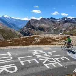 Cyclist enjoying Alpine climb with Tour de France road graffiti and mountain backdrop on Marmot Tours guided cycling tour of French Alps