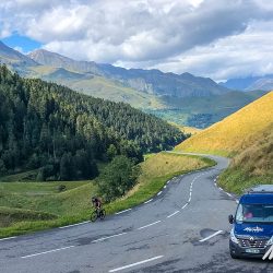 Cyclist enjoying a climb with mountain backdrop and Marmot Tours support van on Raid Pyrenees cycling challenge