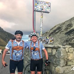 Two cyclists smiling in lederhosen cycling jerseys at the summit of Col du Tourmalet on Marmot Tours guided road cycling challenge Pyrenees France