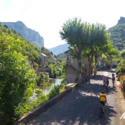 Group of cyclists riding through village with river on Marmot Tours guided road cycling holiday south of France Cevennes and Ardeche