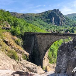 Cyclists crossing bridge over gorge on guided road cycling holiday south of France Cevennes and Ardeche region