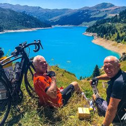 Pair of cyclist enjoying a rest with views of Lac Roselend on Marmot Tours road cycling challenge Raid Alpine