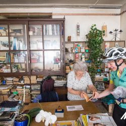 Female cyclist having carnet stamped by elderly lady on Marmot Tours Raid Massif Central French cycling holidays