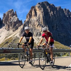 Pair of smiling cyclists with Dolomites backdrop on Marmot Tours full support cycling tour Italy