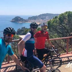 Group of cyclists smiling in sunshine on coast road Tossa de Mar on Marmot Tours guided cycling tour Girona Catalonia Spain with full support