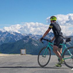 Cyclist scanning mountain views before descending Col d'izzard on supported road cycling mini break in Alps with Marmot Tours