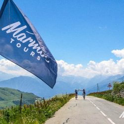 Marmot Tours guided waving flag on Col de la Madeleine for approaching cyclist on guided road cycling mini break