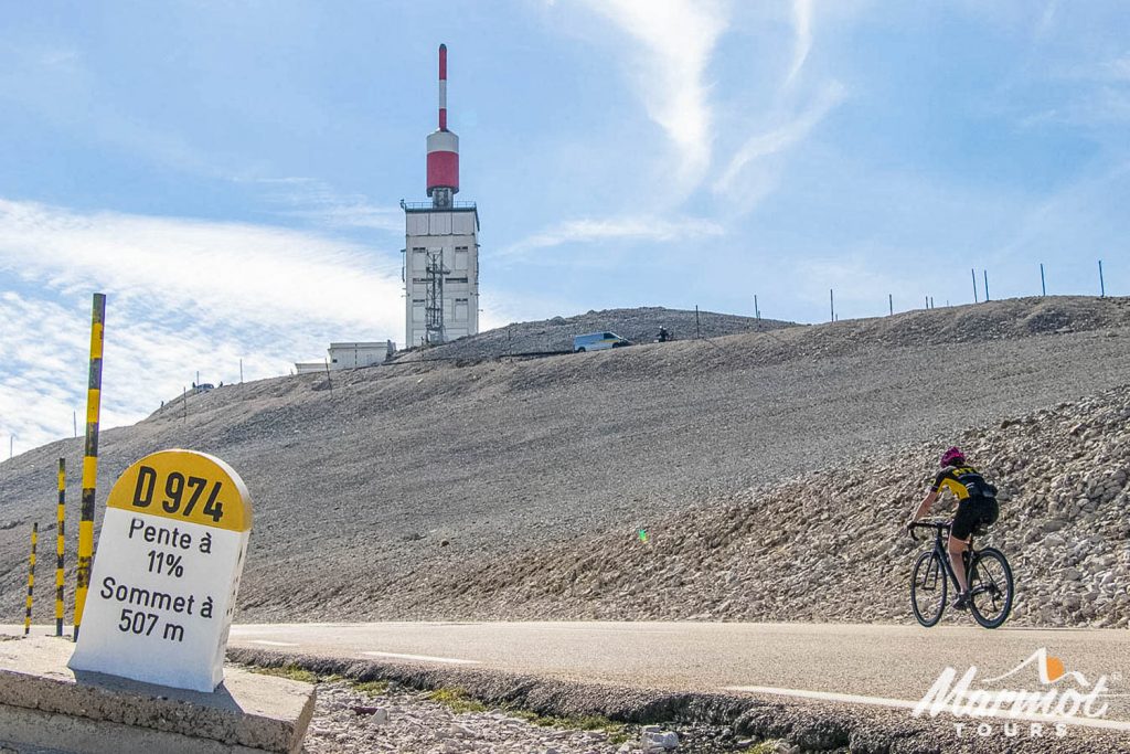Cyclist nearing summit of Mont Ventoux with road marker in foreground on Marmot Tours guided road cycling holiday Mont Ventoux Provence