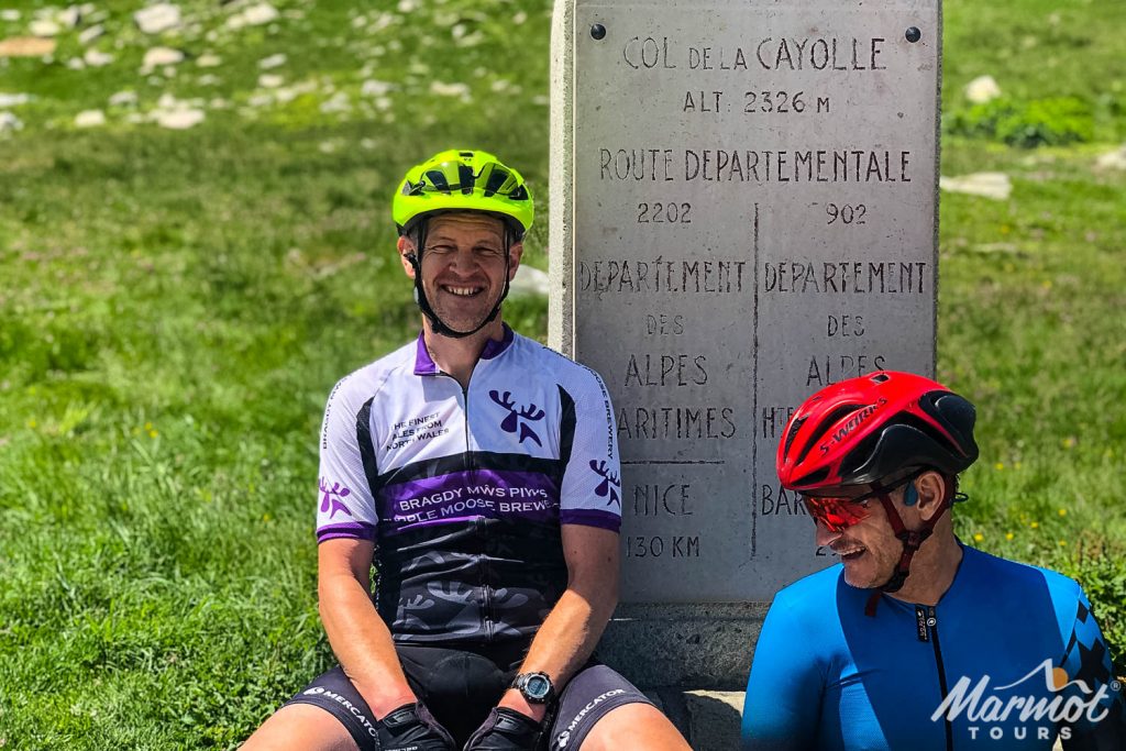 Pair of smiling cyclists posing at Col de la Cayolle sign on Marmot Tours guided road cycling tour of southern alps