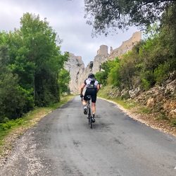 cyclist climbing to chateau ruins in foothills pyrenees with marmot tours