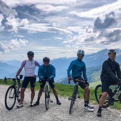 Group of cyclists posing with Alpine peaks in background on guided road cycling tour of French Alps with Marmot Tours