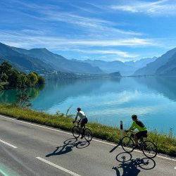 Pair of cyclist riding alongside lake and mountains on Grosse Scheidegg loop Swiss Alps with Marmot Tours