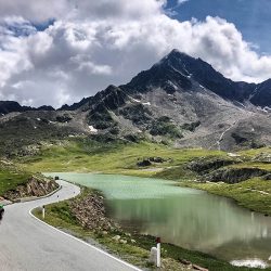 Cyclist riding alongside lake with mountain backdrop on pass di gave cycling climb on Marmot Tours Raid Dolomites challenge