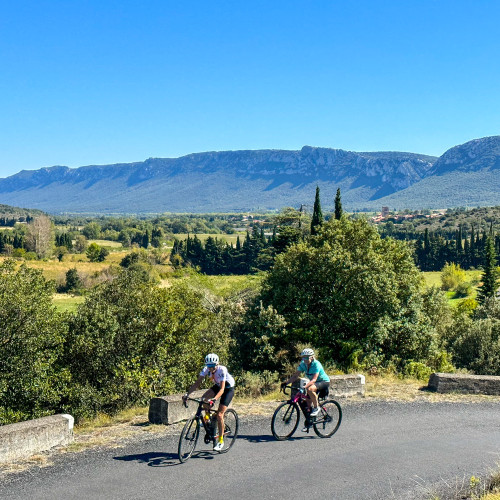Pair of cyclists on remote rural road in pyrenean foothills with peaks in background and rolling meadows on marmot tours cycling holiday