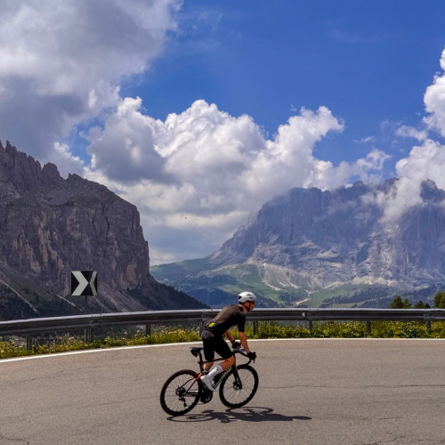 cyclist climbing passo di gardena on raid dolomites with limestone peaks backdrop on marmot tours cycling challenge