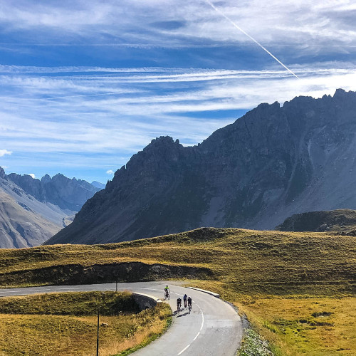Group of cyclists climbing French alps pass surrounded by alpine peaks on raid alpine marmot tours guided cycling challenge