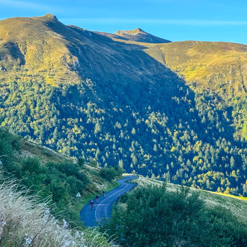 cyclists climbing mountain pass beneath towering Massif Central peaks on road cycling holiday with marmot tours