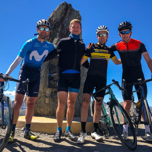 four cyclists pose at col de la bonette sign with alpine peaks backdrop on marmot tours cycling holiday in southern French alps