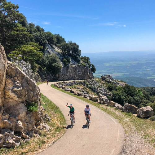 pair of cyclists climbing balcony road with plateau belo and waving on marmot tours Catalonia and girona road cycling tour