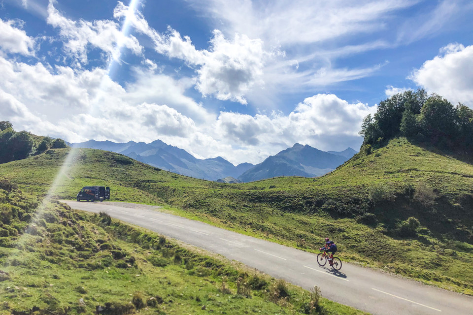 cyclist climbing col d'agnes approaching marmot tours support van with mountain peaks in distance