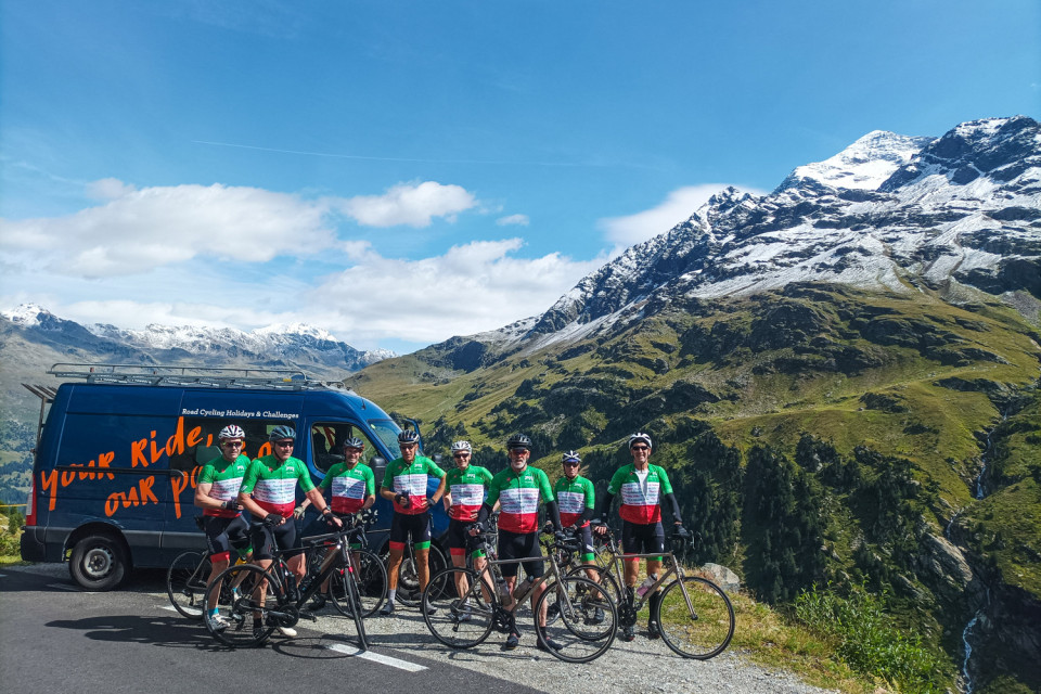 group of cyclists in matching kit and marmot tours support vehicle with mountain backdrop