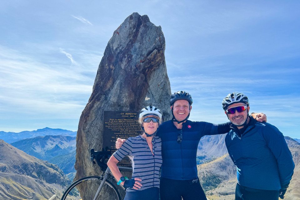 three cyclists pose at col de la bonette with alpine peaks backdrop on marmot tours cycling holiday