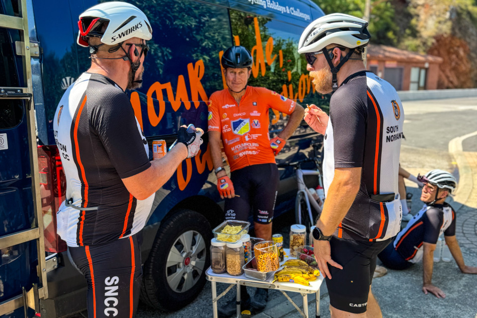 Group of cyclists enjoy snacks provided at marmot tours liveried support vehicle on European road cycling holiday