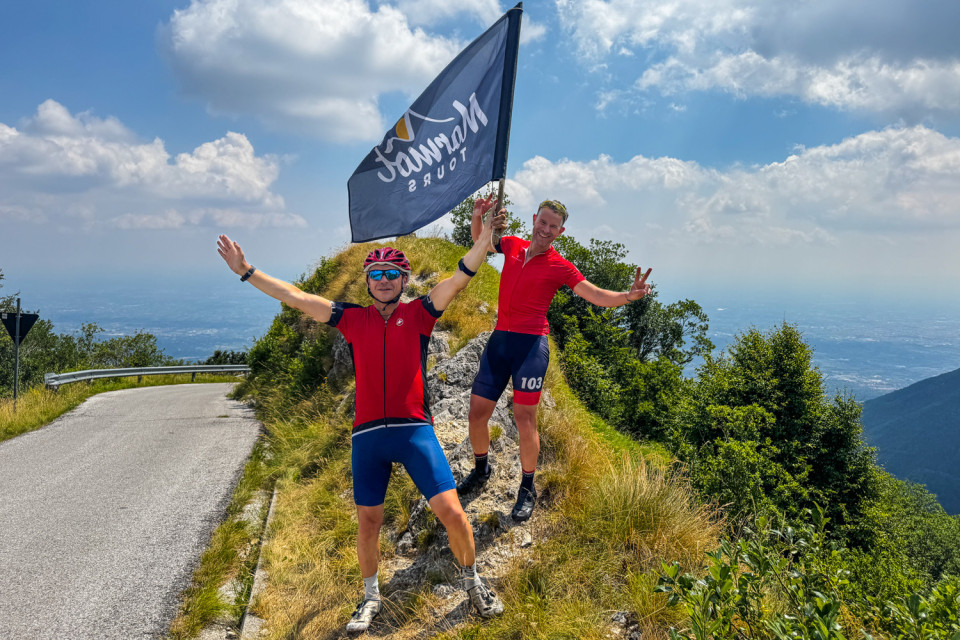 pair of cyclists wave marmot tours flag on goat leap cycling climb southern dolomites