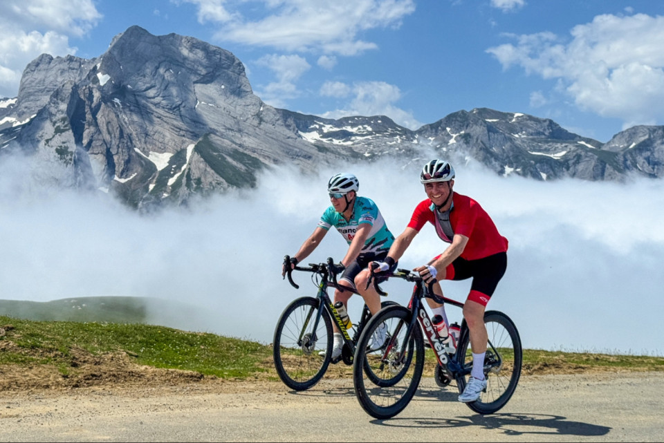 pair of cyclists summiting col D'Aubisque with cloud inversion and mountain peaks backdrop on French pyrenees cycling holiday with marmot tours