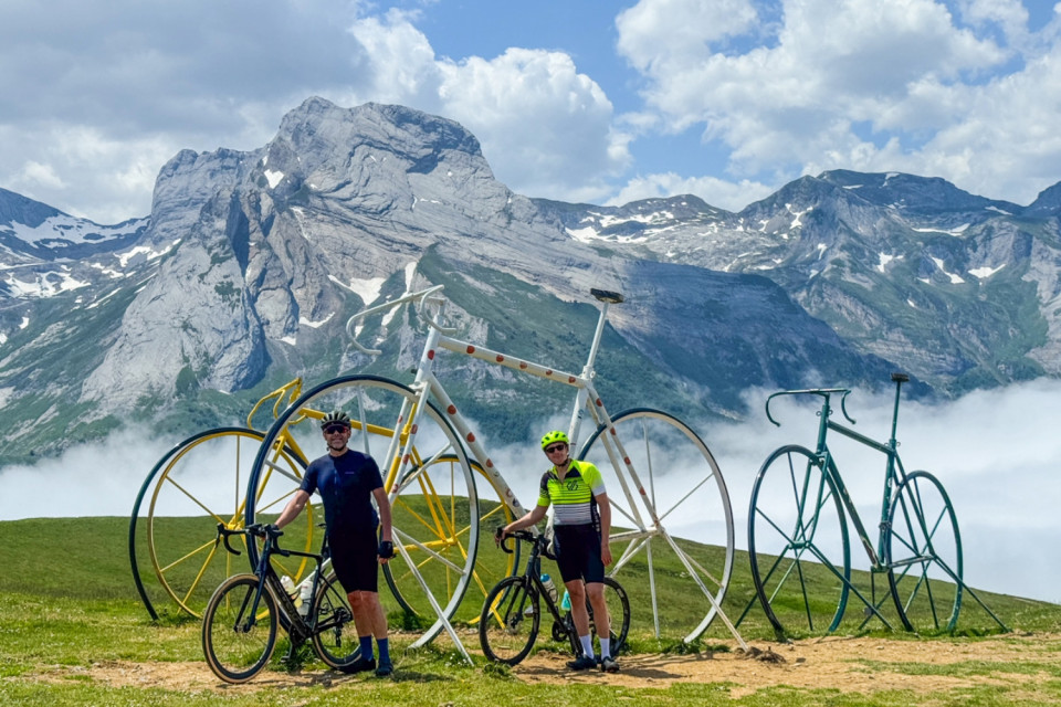 pair of cyclists pose at col D'Aubisque bicycle sculptures on Atlantic to mediterranean cycling challenge with marmot tours