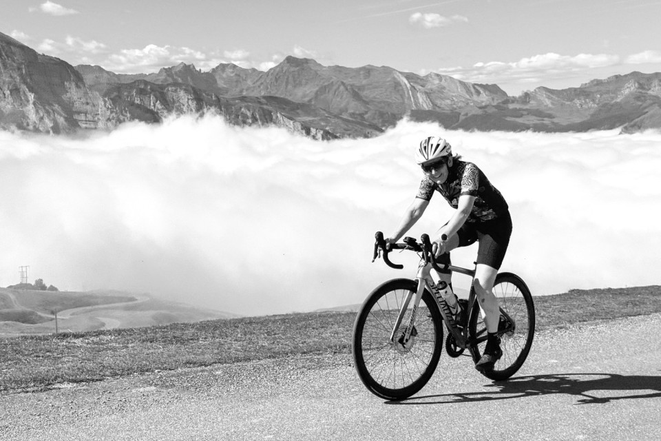 female cyclist summiting col D'Aubisque above cloud inversion on marmot tours raid pyrenees cycling challenge
