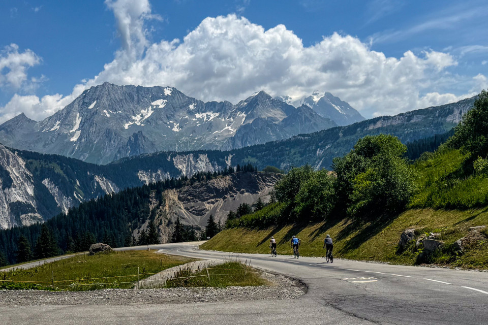 cyclists descending col de la lose cycling climb with French alpine peaks background on marmot tours guided road cycling holiday
