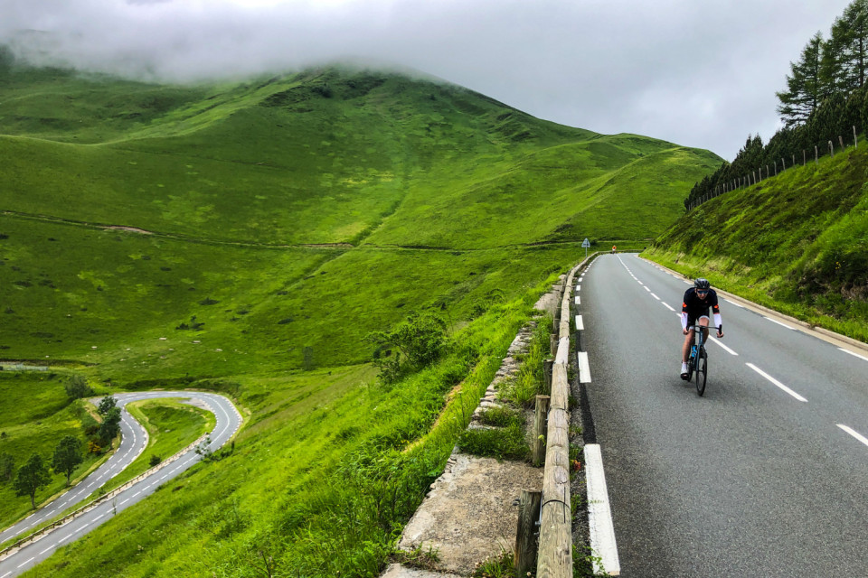 cyclist climbing col de peyresourde cycling climb with green mountain slopes below on marmot tours French pyrenees cycling holiday raid pyrenees