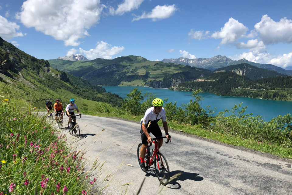 Group of cyclists climbing alongside lake on Cormet de Roselend in Northern French Alps with Marmot Tours guided support cycling holidays