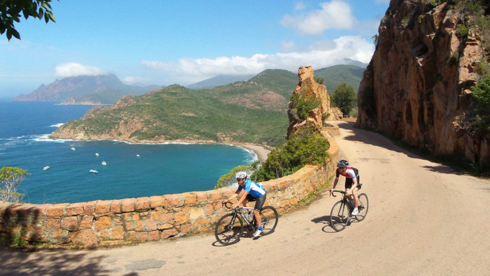 Two road cyclists on spectacular coastal road with mountains of Corsica behind on Marmot Tours supported holiday