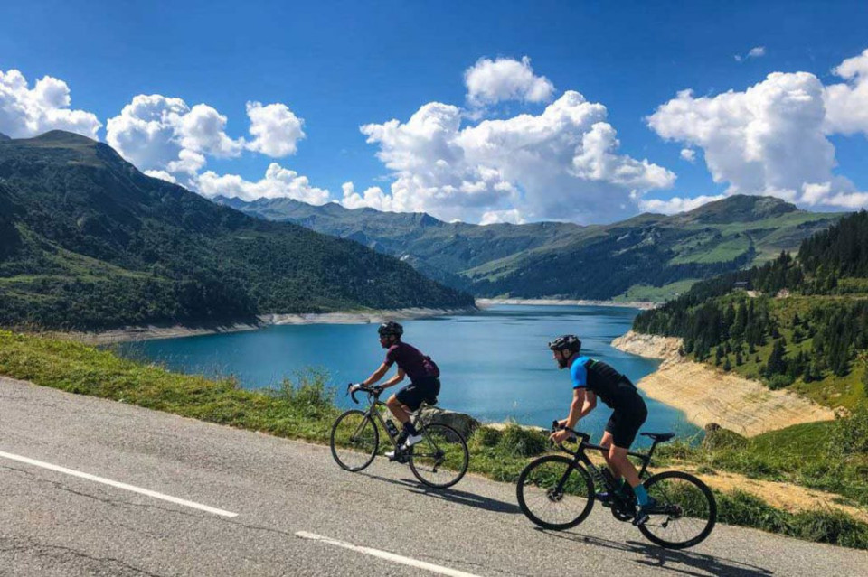 Pair of cyclists climbing Cormet de Roselend with view of lake and mountains on Marmot Tours fully supported road cycling holiday French Alps