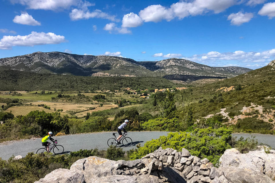 Pair of cyclists climbing in foothills of Pyrenees with hilly backdrop