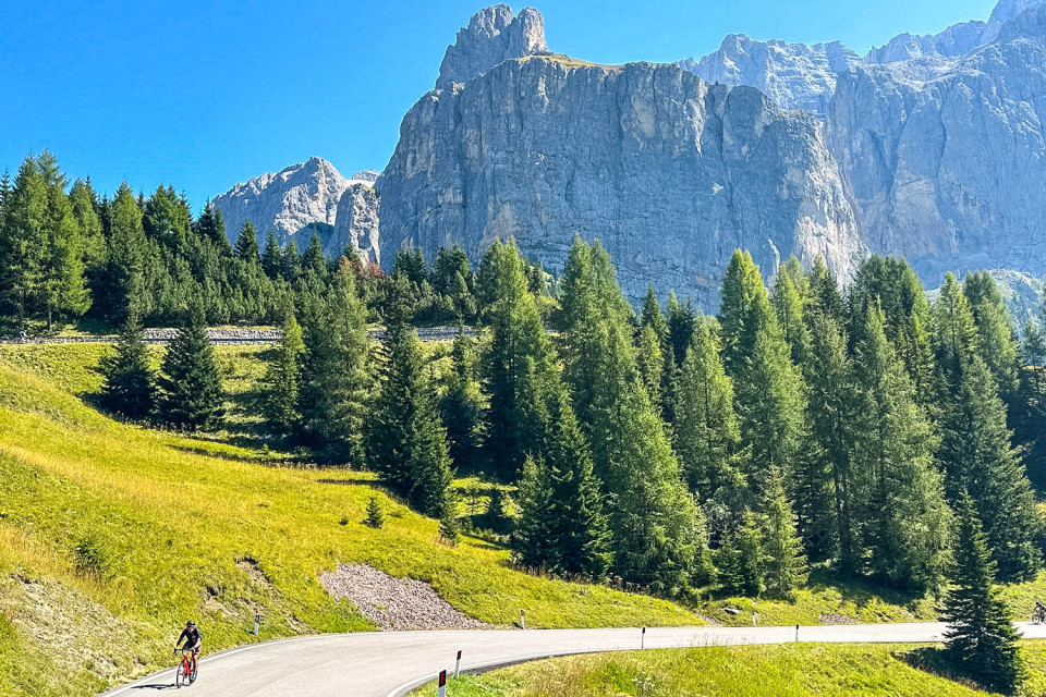 Cyclist climbing Passo Gardena beneath towering limestone peaks on Marmot Tours Raid Dolomites cycling challenge