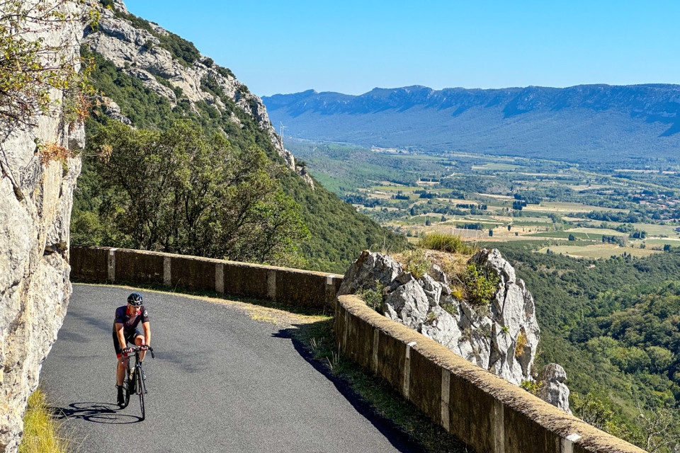 cyclist climbing balcony road with Bailey below in pyrenean foothills on marmot tours French cycling holiday