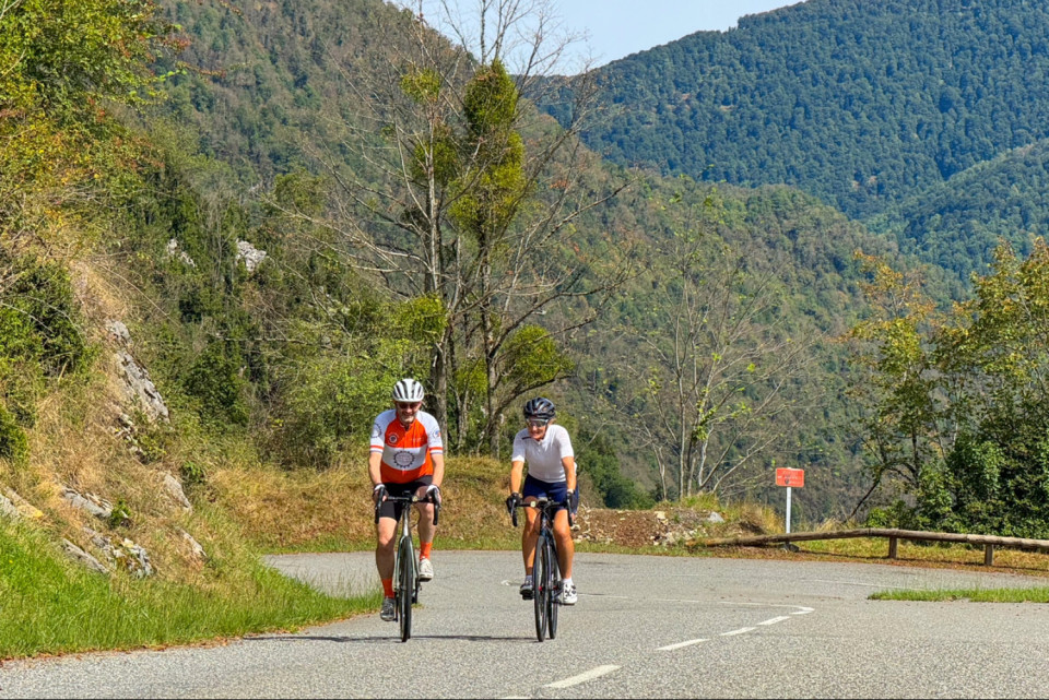 pair of cyclists climbing col de Mente with forested slopes backdrop in French pyrenees on marmot tours road cycling holiday