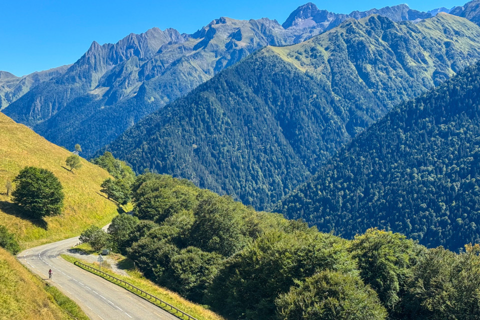 multiple mountain slopes under blue skies with cyclists climbing mountain pass on French pyrenees cycling holiday with marmot tours