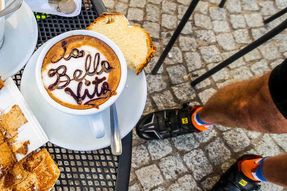 Cappuccino with la Bella Vita in chocolate sprinkles and cyclist's feet on Marmot Tours' guided road cycling tour Sardinia
