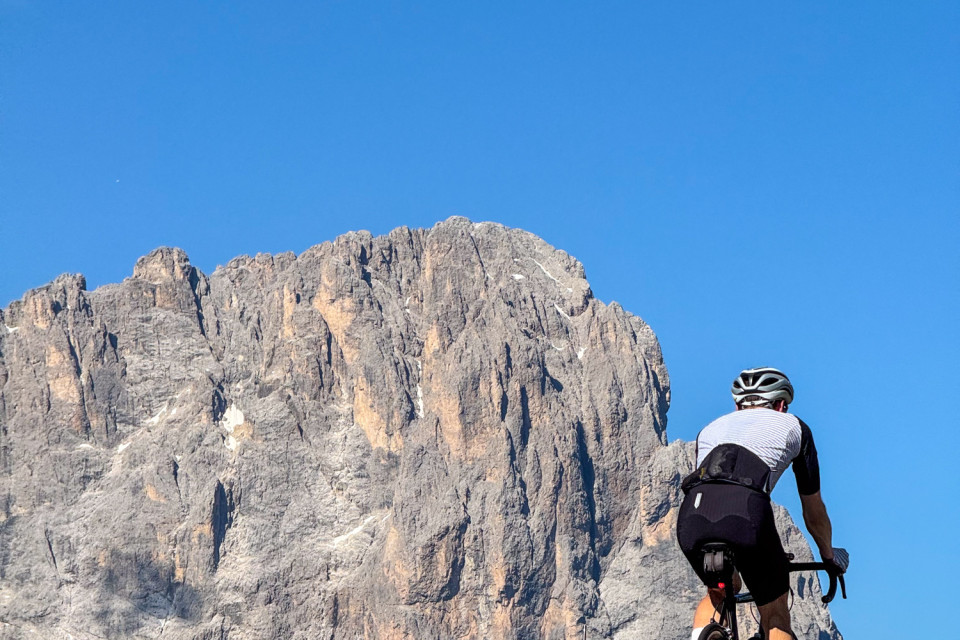 cyclist climbing mountain pass with limestone mountain peaks background against blue sky in Bormio region of Italy on marmot tours guided road cycling holiday