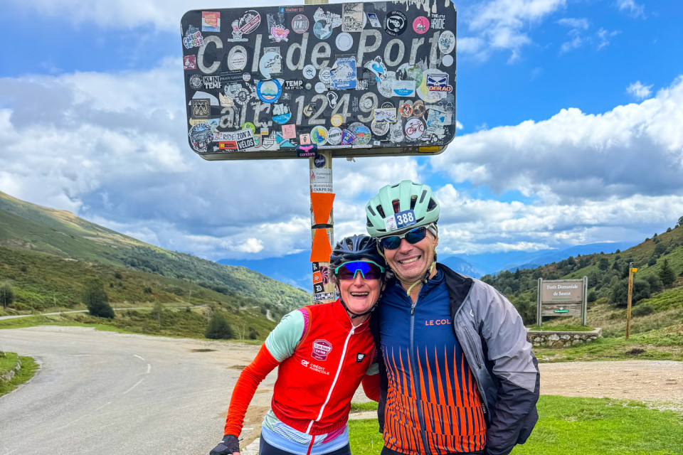Pair of cyclists pose at col de port sign with mountain backdrop on French pyrenees cycling holiday with marmot tours