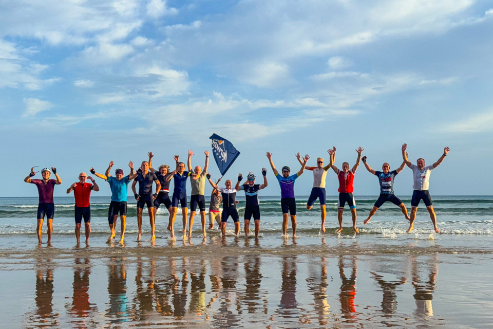 group of cyclists jump for joy at shore of Hendaye on day 1 of raid pyrenees cycling challenge with marmot tours